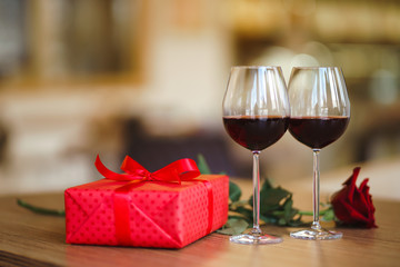 Valentine's day celebration concept. Two glasses of wine, red rose red gift box on wooden table. Romance at restaurant. Valentine's Day, holiday concept. Relationship, surprise and love concept.