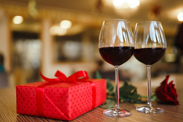 Valentine's day celebration concept. Two glasses of wine, red rose red gift box on wooden table. Romance at restaurant. Valentine's Day, holiday concept. Relationship, surprise and love concept.