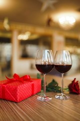 Valentine's day celebration concept. Two glasses of wine, red rose red gift box on wooden table. Romance at restaurant. Valentine's Day, holiday concept. Relationship, surprise and love concept.