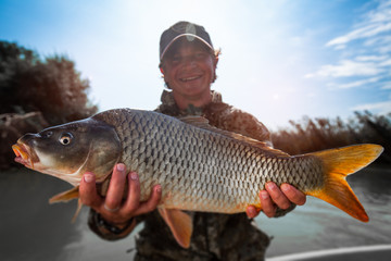 Happy fisherman holds the big Carp fish (Cyprinus carpio) and smiles