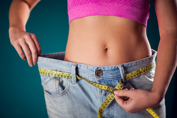 Woman wearing big size jeans with meter on the belt. Weight loss and diet concept
