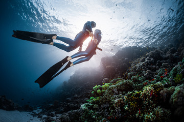 Two freedivers swim over the vivid coral reef in a tropical sea during their recreational freedive session