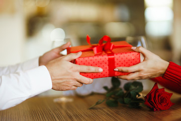 Valentine's Day, holiday and surprise concept. Man gives to his woman a red gift box. Sweet couple celebrate their anniversary. Relationship and love concept.