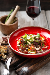 Warm beef liver salad with arugula, lettuce and tomatoes on a red plate. A delicious gourmet dinner in the rustic style