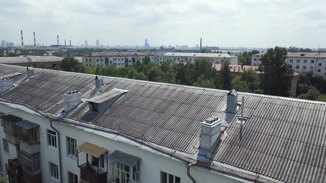Aerial view of multistory apartment buildings in green residential area. Stock footage. Flying over the roofs of old houses surrounded by trees on cloudy sky background.
