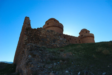 towers of the medieval spanish castle La Calahorra behind the outer wall in the light of the evening sun, Granada, Spain