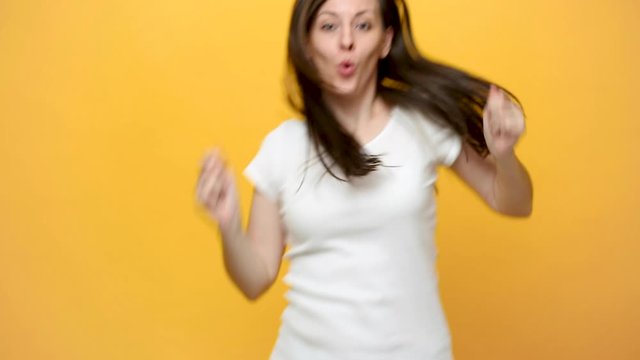 Happy fun crazy young woman in white t-shirt fooling around, dancing, jumping in front of camera, hiding isolated over yellow background in studio. People sincere emotions lifestyle concept. Mock up.