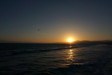 Sun going down behind a surfer and Paraglider off the beaches of Santa Monica, California