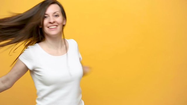 Smiling pretty fun crazy happy brunette young woman in white t-shirt fooling around dancing circling jumping smile isolated over yellow background in studio. People sincere emotions lifestyle concept.