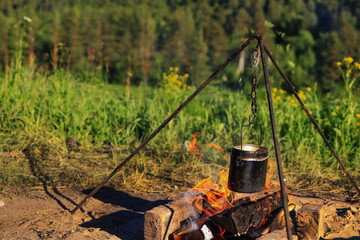 The Metal Cauldron Hanging On A Tripod Over An Open Fire. Tourist pot hanging over the fire on a tripod.