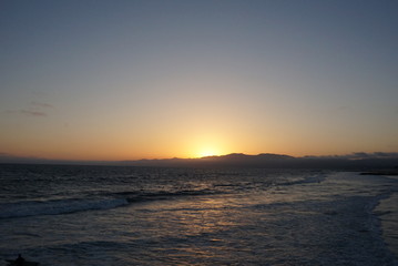 Sunsetting behind the mountains just off the beach of Santa Monica, California with a surfer and paraglider enjoying the views