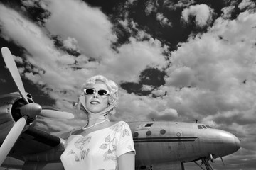 Woman in retro outfit in front of antique propeller airplane