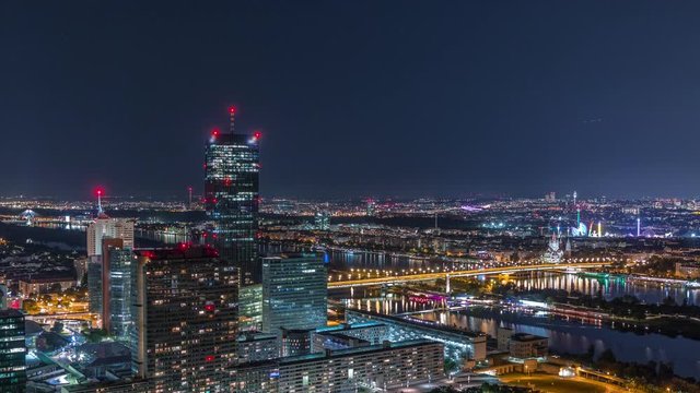 Aerial panoramic view over Vienna city with Donau City skyscrapers, historic buildings and a riverside promenade night timelapse in Austria. Illuminated skyline from Danube Tower viewpoint