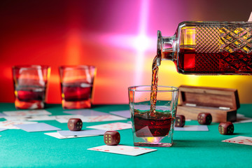 Casino table with cards and dice . Whisky is poured into a glass from a decanter .