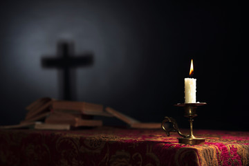 Burning candle on a dark background with the silhouette of the cross.