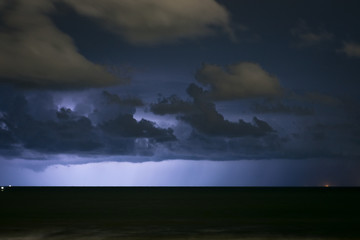 Naklejka na ściany i meble Clouds are illuminated by lightning from a thunderstorm over sea