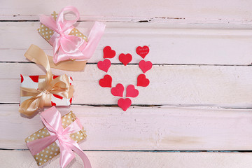 Greeting card for Valentine's Day or Women's Day. Red hearts on a pink wooden background and gift boxes with ribbon, flat lay. Happy holiday, place for text, banner for screen