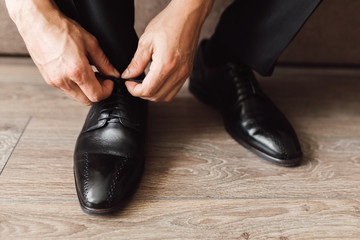 Frontview of man is tying the laces at black shoes on the wooden floor