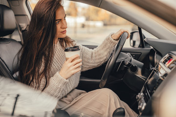 Young pretty woman with smartphone and cup of coffee seat in car