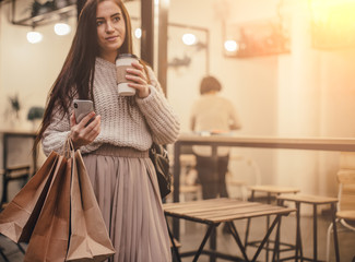 Young trandy woman near street cafe drink coffee with shopping bags