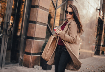 Young pretty woman in coat with shopping bags, cup of black coffee and smartphone
