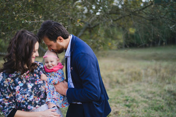 Fototapeta premium Young happy caucasian couple with little baby girl. Parents and daughter walking and having fun together. Mother and father play with child outdoors. Family, parenthood, childhood, happiness concept.