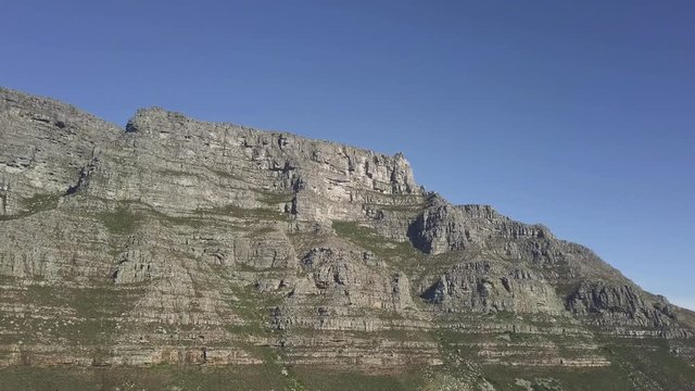 Aerial lower angle scenic drone flight view of Table Mountain in late afternoon sun against blue sky. Steep sand stone cliff and tectonic lines showing erosion and tectonic lines,