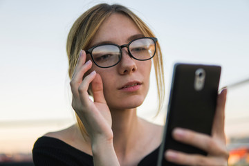 Young business woman uses phone. Good looking brunette female uses online banking on smart phone to transfer money from credit card. Girl using smart phone and chatting with business partners.