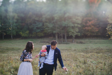 Young happy caucasian couple with little baby girl. Parents and daughter walking and having fun together. Mother and father play with child outdoors. Family, parenthood, childhood, happiness concept.