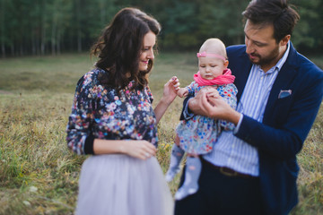 Fototapeta premium Young happy caucasian couple with little baby girl. Parents and daughter walking and having fun together. Mother and father play with child outdoors. Family, parenthood, childhood, happiness concept.