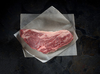 fresh raw marbled beef steak on parchment paper on a dark background