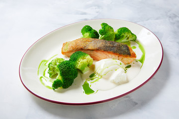 cooked broccoli with baked red fish, with sauce, laid out on a white plate