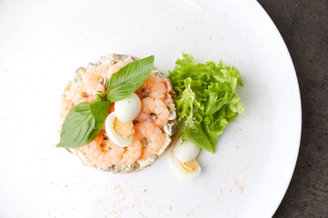vegetable salad decorated with shrimp and quail boiled eggs, on a white plate