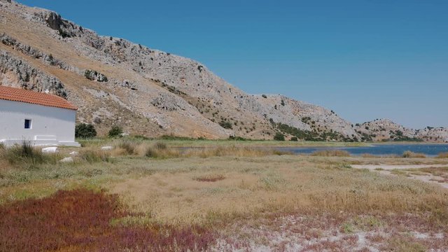 A small white church - Chapel St. Peter on the background of rocks near the Prokopou lagoon and the village of Kalogria, Northwest Peloponnese, Greece. PAN to left