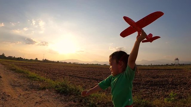 Slow motion of a happy little child girl runs with a toy airplane on a sunset background over a field. Concept of happy family and childhood dreams.