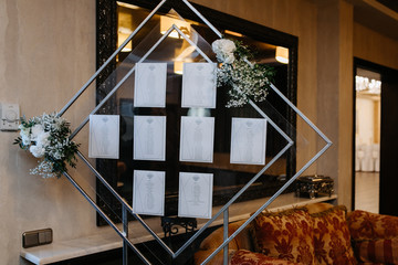Glass plate with table numbers and guests names decorated with flowers at the restaurant hall