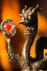 A small statue of a Chinese Dragon holding an orb with Flames in the Background
