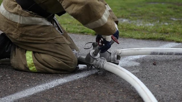 Close up of a fireman with hose splitter and fire hoses, unscrews the valves