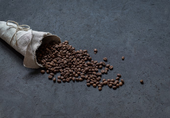 Black coffee beans scattered from a bag of flax on a dark background