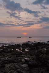 Colorful Thai red sunset, blue clouds calm sea, 2 fisherman boats on the horizon, stone beach