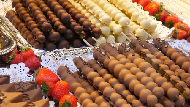 Various fruits on a wooden skewer stick in a caramelized glaze made of milk black white chocolate. Grapes, banana, strawberries in icing on the counter of the Christmas market