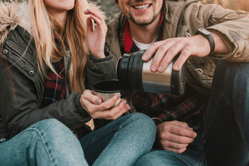 Travel couple camping with thermos having fun in the forest. Concept of trekking, adventure and seasonal vacation.