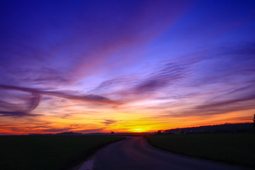 Beautiful multicolored sunset. Cumulonimbus and very colorful stratus in a dramatic sky. Sun disappearing behind a hill.