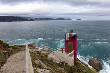 The very small lighthouse Viveiro in northern Spain on the Atlantic coast of Galicia. Solar panels supply the electricity. In the background the Atlantic Ocean with dark clouds in the sky.