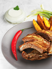 Grilled ribs with idaho potatoes and vegetables on the plate, on the grey background. Shallow depth of field. Vertical orientation, close-up.