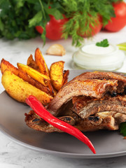 Grilled ribs with idaho potatoes and vegetables on the plate, on the grey background. Shallow depth of field. Vertical orientation, close-up.