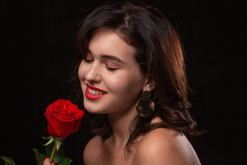 Beautiful woman with bright makeup posing isolated over black background with red rose.