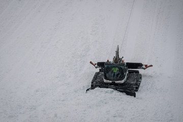 Snow groomer working on a very steep terrain, using a winch and a rope as a security guard. Groomer...