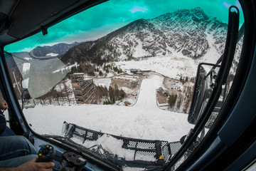 Interior of a cabin of snow groomer while working on a steep slope going downhill. Groomer going downhill while being attached to a steel wire. Hand on the controls is visible.