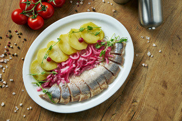 Norwegian slightly salted herring with baked potatoes, tomatoes and pickles on a white plate. Classical Ukrainian antipasti. Top view food on wooden background